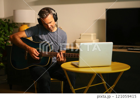 A man sitting in front of the computer practicing online music lessons A man sitting in front of the computer practicing online music lessons 121059415