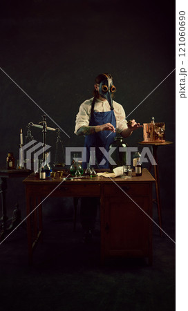 Carefully measuring herb into large jar, plague doctor appears to be creating tincture or infusion, surrounded by classic laboratory tools. Carefully measuring herb into large jar, plague doctor appears to be creating tincture or infusion, surrounded by classic laboratory tools. 121060690
