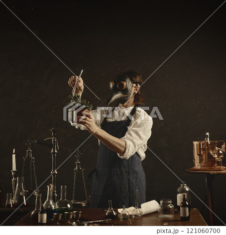 Carefully measuring spice or herb into large jar, plague doctor appears to be creating tincture or infusion, surrounded by classic laboratory tools. Carefully measuring spice or herb into large jar, plague doctor appears to be creating tincture or infusion, surrounded by classic laboratory tools. 121060700