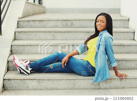 Fashion happy smiling young african woman wearing a jeans clothes sitting resting on stairs Fashion happy smiling young african woman wearing a jeans clothes sitting resting on stairs 121060802