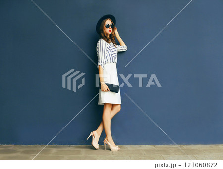 Fashion elegant woman in a black hat and white skirt with a handbag clutch over a gray background Fashion elegant woman in a black hat and white skirt with a handbag clutch over a gray background 121060872