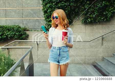 Stylish smiling young woman using smartphone with coffee cup in the city Stylish smiling young woman using smartphone with coffee cup in the city 121060888