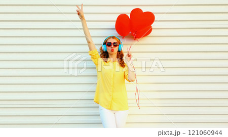 Happy young woman with red heart balloons listening to music in headphones on white background Happy young woman with red heart balloons listening to music in headphones on white background 121060944