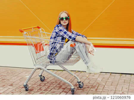 Fashion cool girl sitting in shopping trolley cart over colorful background Fashion cool girl sitting in shopping trolley cart over colorful background 121060976