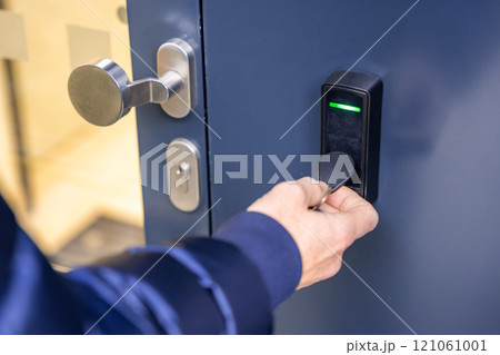 Close up view of person using a electric lock key fob to access a building via a reader of entry system mounted on a house wall 121061001