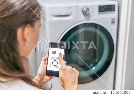 Young woman using mobile phone control via wi-fi and app for washing machine in home. Homesmart and new technology concept 121061005
