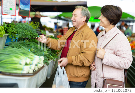 Positive mature male and female picking dill at local grocery bazaar Positive mature male and female picking dill at local grocery bazaar 121061072