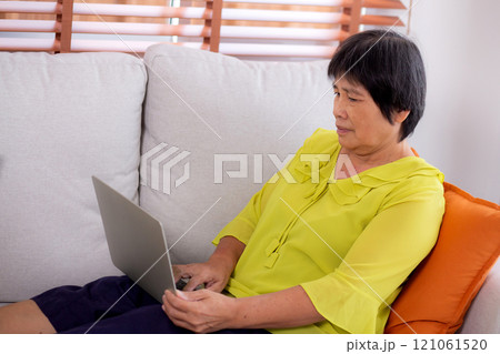 Asian senior woman sitting on sofa using laptop computer for looking social media in living room. Asian senior woman sitting on sofa using laptop computer for looking social media in living room. 121061520