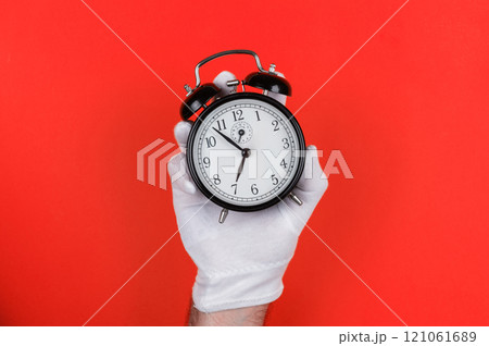 Gloved Hand Holding Black Alarm Clock on Red Gloved Hand Holding Black Alarm Clock on Red 121061689