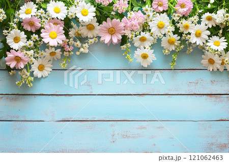 A old wooden plank background with a variety of yellow and white flowers, including daisies on the sides.  121062463