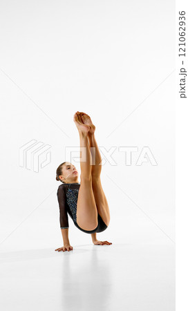 Female gymnast, artistic sportsman maintains strong focus, improving flexibility and control against white studio background. Copy space. 121062936
