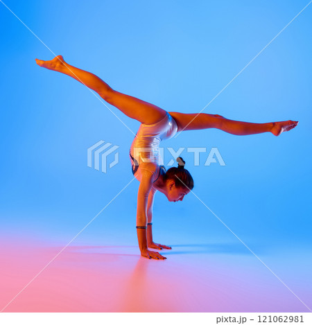 Young gymnast, flexible girl dressed festive costume performing handstand in pink neon light against gradient blue background. Young gymnast, flexible girl dressed festive costume performing handstand in pink neon light against gradient blue background. 121062981