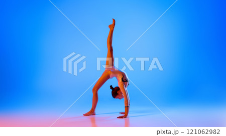 Showcasing strength and poise, gymnast performs flawless handstand, in pink neon light against gradient blue background. 121062982
