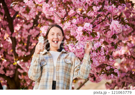 Woman allergic suffering from seasonal allergy at spring. Young happy woman applying allergy drug, posing in blossoming garden at springtime. Antihistamine medication concept Woman allergic suffering from seasonal allergy at spring. Young happy woman applying allergy drug, posing in blossoming garden at springtime. Antihistamine medication concept 121063779