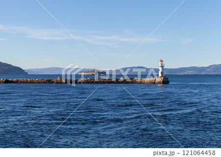 Lighthouse tower is mounted at the end of stone breakwater 121064458