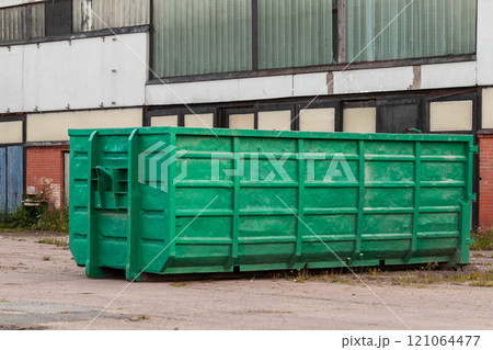 Green trash container standsnear concrete wall 121064477