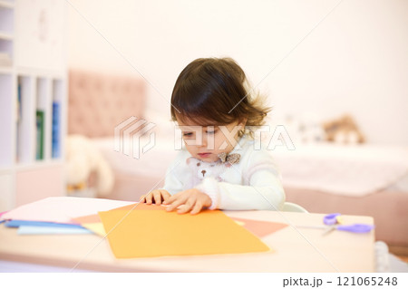 little child girl holding multi-color paper while sitting by table at home, Children creativity 121065248