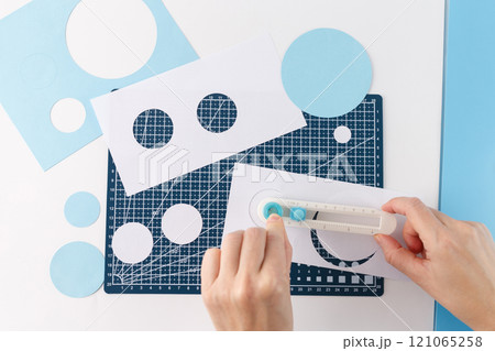 top down view hands using manual rotary cutting tool for cut out paper circle in different size, a blue background, and there are several cut-out circles of different sizes scattered around, top down view hands using manual rotary cutting tool for cut out paper circle in different size, a blue background, and there are several cut-out circles of different sizes scattered around, 121065258