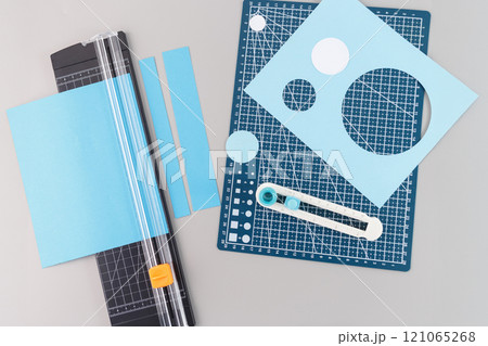 a collection of crafting tools and materials used for cutting circles. There is a blue cutting mat with a grid and various measurement markings, circular cutouts, and a paper trimmer tool, top view, 121065268