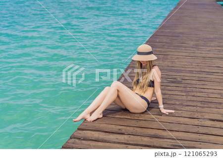 Woman in swimsuit sitting on a pier at Lake Bacalar. Quintana Roo, Mexico travel, summer relaxation, and waterfront serenity concept Woman in swimsuit sitting on a pier at Lake Bacalar. Quintana Roo, Mexico travel, summer relaxation, and waterfront serenity concept 121065293