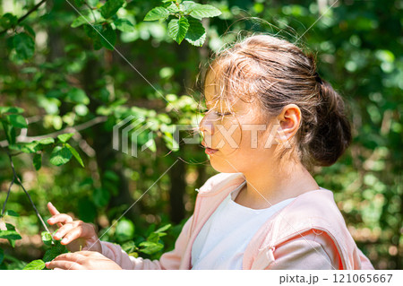 A young school girl in white and pink standing in lush green foliage  121065667