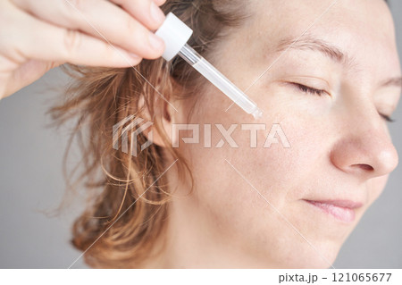 Caucasian female applying skincare serum with dropper on face for healthy young 121065677