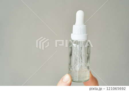 Clear dropper bottle with serum held by caucasian female hand against a neutral 121065692