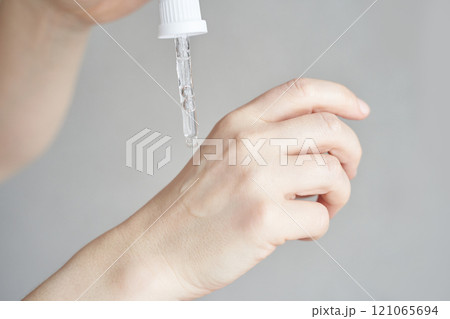 Close up of female hand applying skincare serum with dropper on light background 121065694