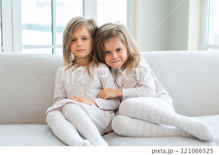 Happy family sisterly love. Two funny little twin sisters girls hugging with love care playing together at home indoors. Happy children lifestyle. Identical twin girls hugs. Girls friendship and youth 121066525