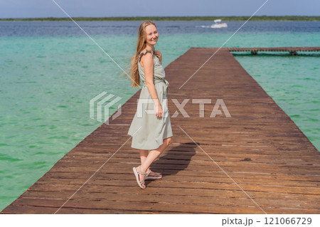 Female tourist in a turquoise dress standing on a wooden pier over the turquoise waters of Bacalar Lake, Mexico. Peaceful tropical travel destination concept Female tourist in a turquoise dress standing on a wooden pier over the turquoise waters of Bacalar Lake, Mexico. Peaceful tropical travel destination concept 121066729