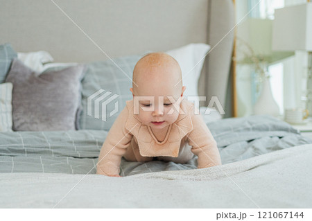 Happy baby. Cute little newborn girl with smiling face crawling on bed in bedroom. Infant baby resting playing lying down on blanket at home. Motherhood happy child childcare concept 121067144