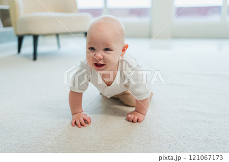 Happy baby. Cute little newborn girl with smiling face crawling on floor in bedroom. Infant baby resting playing in living room indoor at home. Motherhood happy child childcare concept Happy baby. Cute little newborn girl with smiling face crawling on floor in bedroom. Infant baby resting playing in living room indoor at home. Motherhood happy child childcare concept 121067173