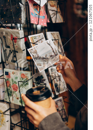A person holds a coffee cup in front of a postcard display 121067505