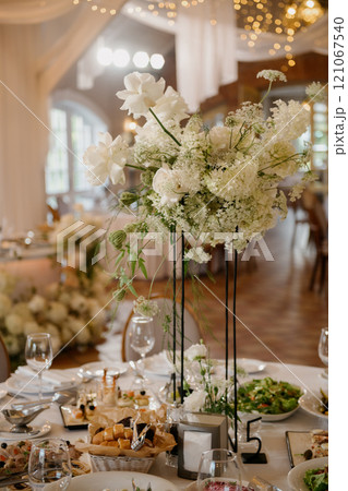 A wedding reception table with white flowers in tall vases 121067540