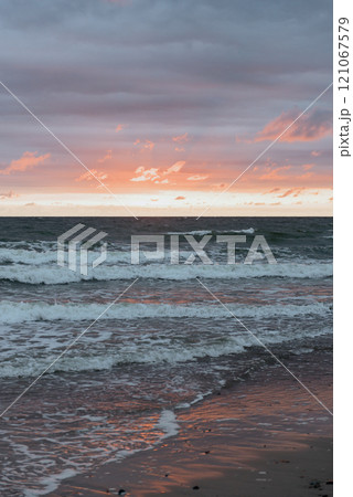 A sunset over the ocean with waves gently crashing on the beach 121067579