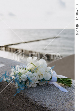 A bouquet of white flowers sits on a ledge by the ocean A bouquet of white flowers sits on a ledge by the ocean 121067594