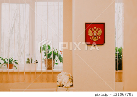 A red coat of arms hangs elegantly on a wall by a window 121067795