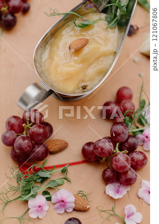 A spoon of sauce surrounded by grapes and flowers on a table 121067806