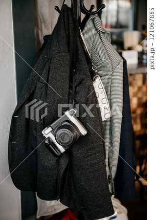 A camera is hanging on a coat rack right next to a jacket A camera is hanging on a coat rack right next to a jacket 121067885