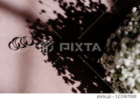 Wedding rings are on a table next to a bouquet of flowers 121067888