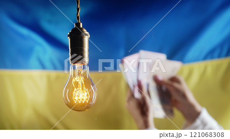 Glowing Edison Light Bulb On Ukrainian Flag. Woman Counting Hryvnias, Ukraine. 121068308