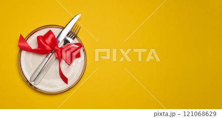Round white plate and tied with red bow view with knife on yellow background, festive table setting Round white plate and tied with red bow view with knife on yellow background, festive table setting 121068629