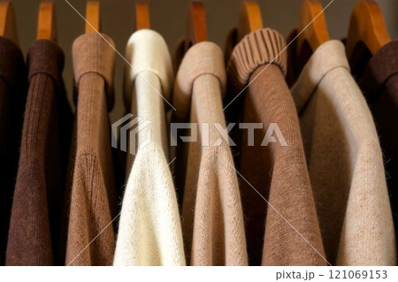 Close-up of hangers with Woolen Sweaters in a row. Sweaters in the closet, in brown and beige colors. Concept of Trendy wardrobe and fashion 121069153