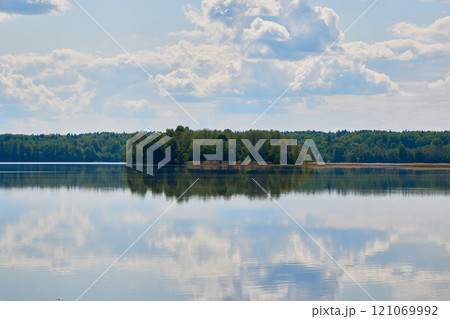A serene lake with stunning reflections of a lush green island beneath a cloudy sky 121069992