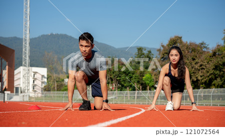 Two determined Asian runners in the starting position, ready to race on a racetrack at a stadium. 121072564
