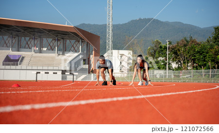 Two determined Asian athlete runners are on the track, getting ready to race in a stadium. 121072566