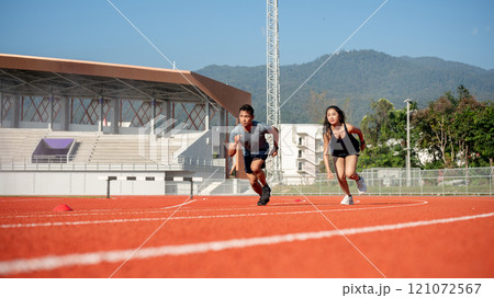 Two determined Asian athletes running on a track in a stadium on a sunny day. 121072567