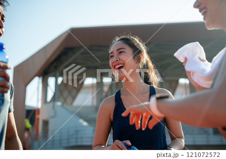 A happy Asian female athlete enjoys a conversation with her friends while resting after training. 121072572