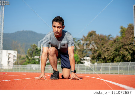 A strong Asian athletic male runner in sportswear trains at a stadium, preparing to run 121072687