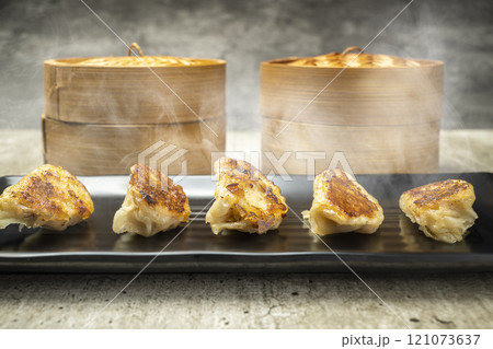 Fried chinese dim sum dumpling, gyoza, jiaozi or mandu in the plate with a bamboo wooden basket bowl on the table. Food for breakfast, lunch or dinner 121073637